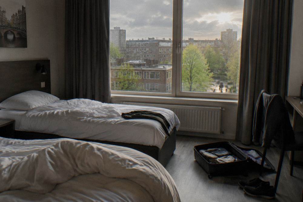 A budget hotel room with twin beds and a city view window